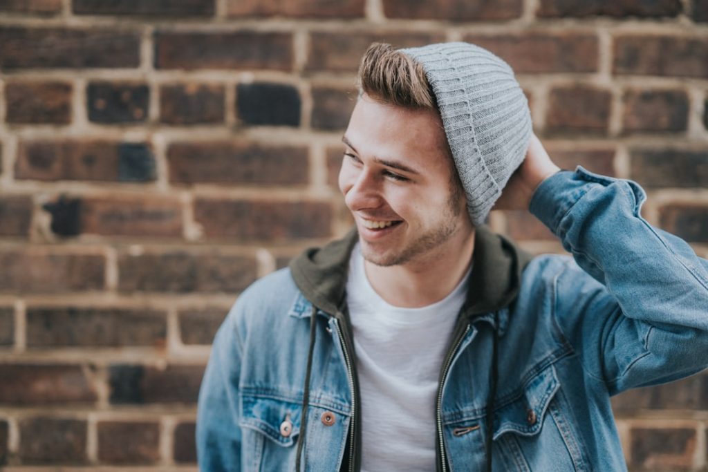 man-holding-the-back-of-his-head-while-smiling-near-brick-wall-ix9i7kfmpcc